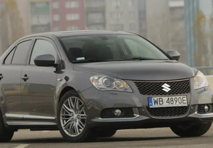 Szary Suzuki Kizashi z polskimi tablicami WB 4890E zaparkowany na tle bloków mieszkalnych.