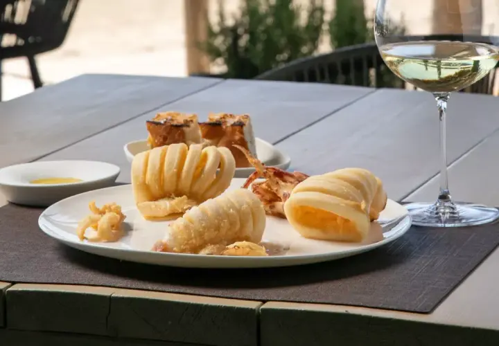 Deliciosa fritura de pescado, calamares crujientes y anillas de calamar, acompañados de pan tostado y una copa de vino blanco.