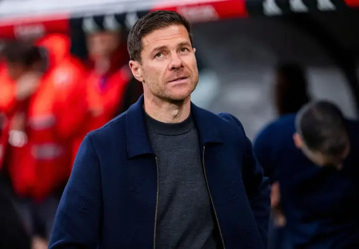 Xabi Alonso, potencjalny trener Chelsea, w granatowej kurtce i szarym swetrze, z uwagą obserwuje boisko.