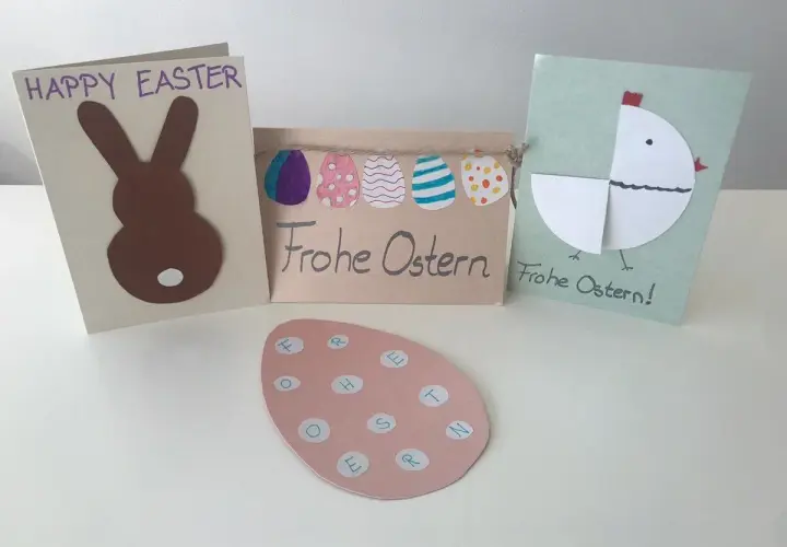 Osterkarten basteln einfach: Hase, Küken und bunte Eier. Ein rosa Ei mit Buchstaben für "Frohe Ostern" liegt vorne.
