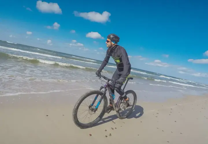 Rowerzysta przemierza piaszczyste plaże Słowińskiego Parku Narodowego. W tle błękitne niebo i fale Bałtyku.