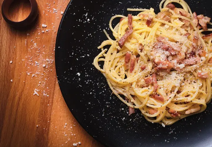 Un plat de spaghetti à la carbonara, garni de lardons et de parmesan râpé, prêt à être dégusté. Parfait pour des recettes pâtes à la carbonara.