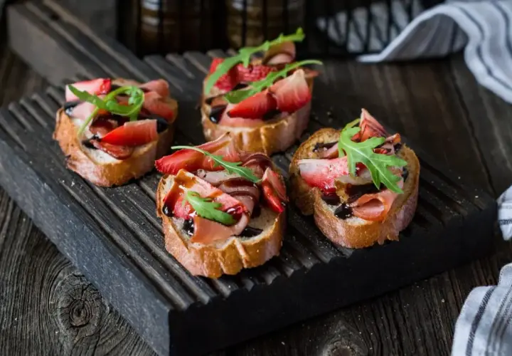 Bruschetta z truskawkami i szynką prosciutto, polana balsamicznym sosem. Idealny przepis na letnią przekąskę.