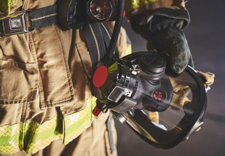 Bombero con equipo de protección, incluyendo una máscara y un compresor de aire respirable.