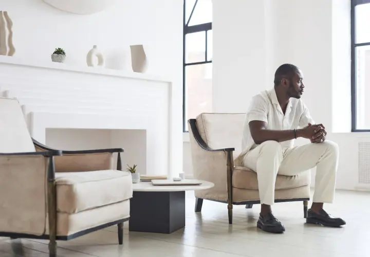 Un homme élégant en tenue claire, assis dans un fauteuil, montre comment porter des mocassins avec style.