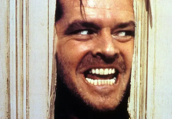 Jack Nicholson, con occhi bianchi e sorriso folle, sfonda una porta. Il suo volto è il **shining significato finale** di un incubo.