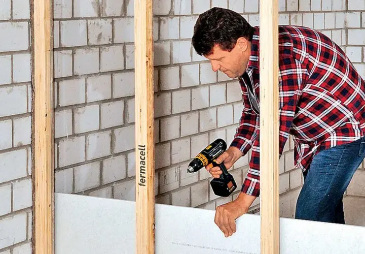 Mann baut eine Trockenbauwand mit Akkuschrauber und Gipskartonplatten.