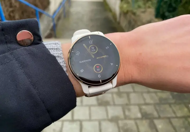 Biały zegarek Garmin na nadgarstku, z widocznym tętnem i liczbą kroków.