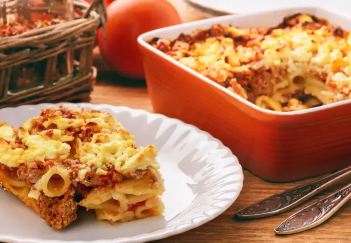 Zapiekanka makaronowa z mięsem mielonym w sosie śmietanowym, podana na talerzu, obok naczynia żaroodpornego.