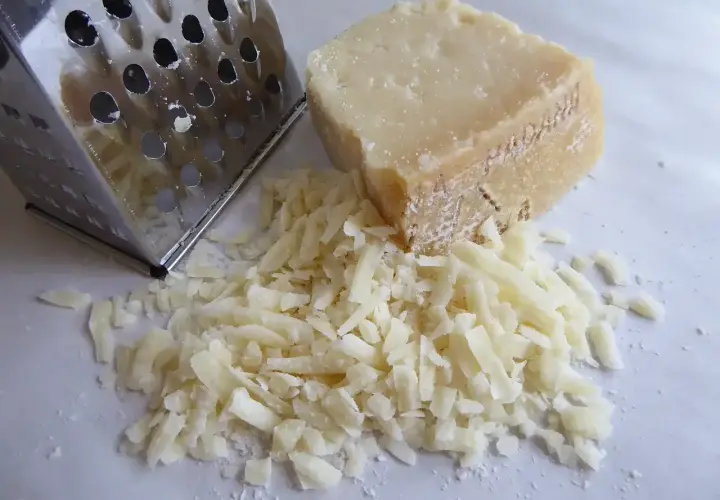 Tarty kawałek Grana Padano i świeżo starty ser obok tarki. Wskazówka, jak przechowywać Grana Padano, aby zachował świeżość.