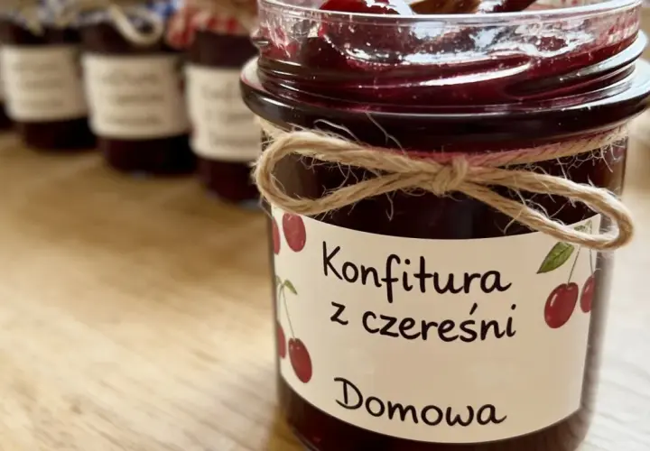 Słoik z domową konfiturą z czereśni, ozdobiony sznurkiem i etykietą z rysunkiem owoców.