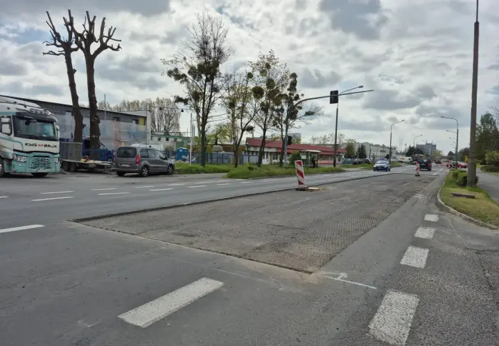 Droga w Opolu z widocznymi pracami drogowymi, samochodami i drzewami.