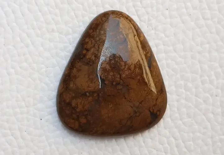 Piedra marrón con vetas oscuras, su significado evoca conexión con la tierra y estabilidad.