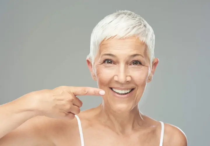 Donna sorridente indica il suo sorriso, un esempio di come rinforzare i denti a cinquant'anni con un sorriso smagliante.