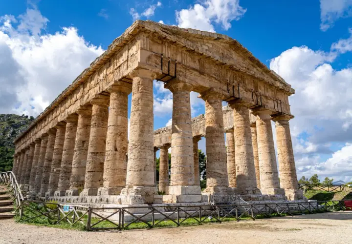 Ancient Greek temple ruins, a highlight of a 2 week Sicily itinerary, stand majestically under a blue, cloudy sky.