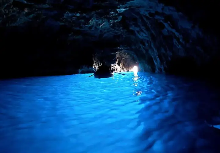 Barca a remi naviga nelle acque azzurre della grotta dello smeraldo, illuminata dalla luce che filtra dall'esterno.