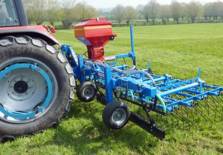 Tracteur rouge avec semoir bleu pour le sursemis de prairie. L'outil prépare le sol avant de semer de nouvelles herbes.