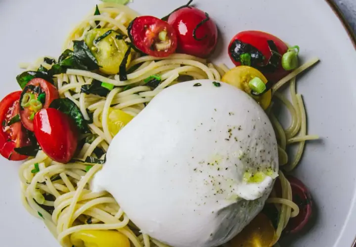 Une belle recette burrata avec des pâtes, des tomates cerises rouges et jaunes, et des herbes fraîches.