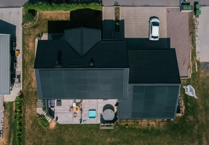 Tak med solceller fångar solens energi. Ett modernt hus med altan, bubbelpool och en vit bil på uppfarten.