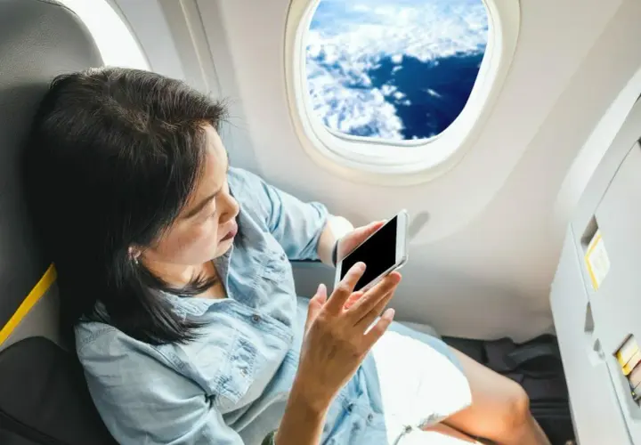 Kobieta z telefonem siedzi przy oknie w samolocie Ryanair, podziwiając widok chmur.