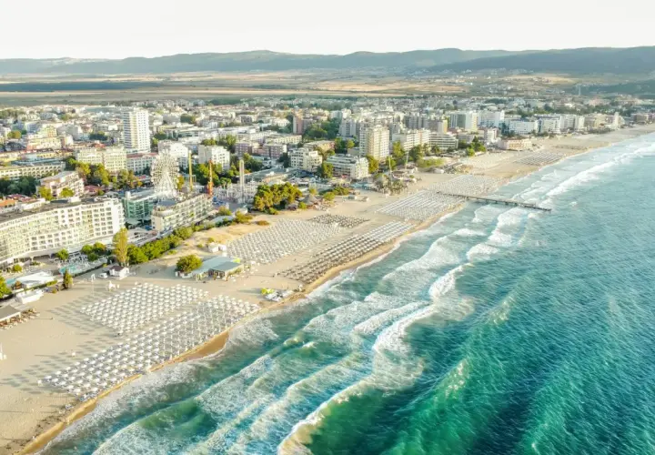 Słoneczne bułgaria plaże z rzędami leżaków i parasoli, turkusowe morze i nadmorskie miasto w tle.