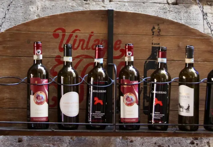 Rząd butelek wina z Toskanii, w tym Chianti Classico i Rosso Montepulciano, prezentuje się na drewnianej półce.