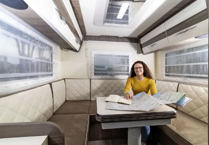 Aménagement du camping car salon arrière : une femme prépare son itinéraire sur une carte.