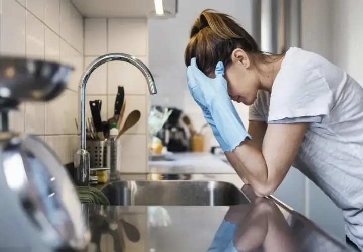 Kobieta w rękawiczkach opiera się o zlew, wyraźnie przygnębiona. Mizofobia utrudnia jej codzienne czynności.