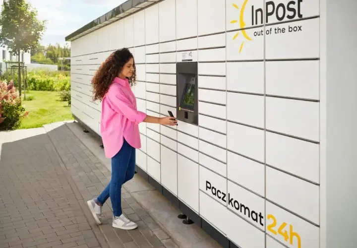 Kobieta z telefonem przy Paczkomacie InPost. Szybka wysyłka InPost za granicę to teraz norma.