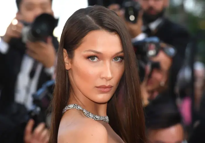 Bella Hadid con un elegante side part, luciendo un collar de diamantes y rodeada de fotógrafos.