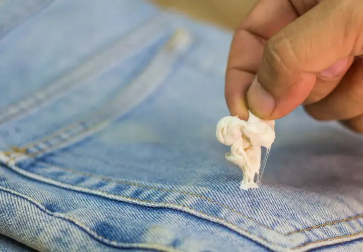 Maintenant, découvrez comment enlever du mastic sur un vêtement. Une main retire une boule de chewing-gum collante d'un jean bleu.