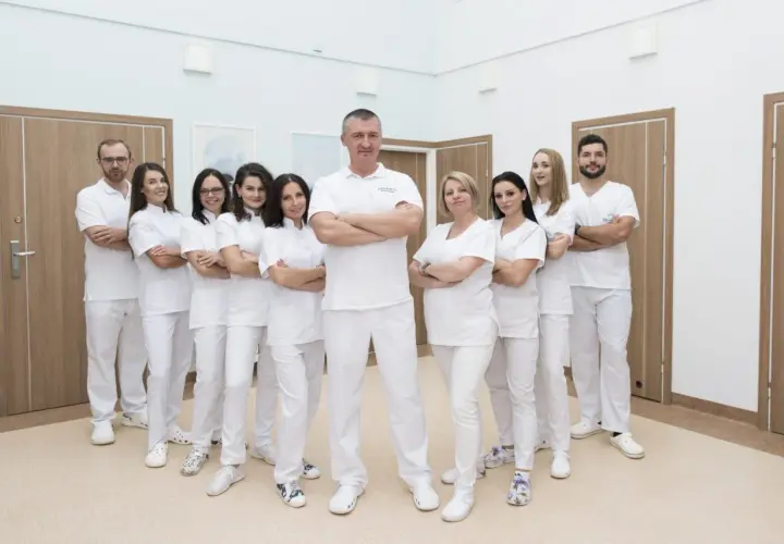 Zespół stomatologów w białych uniformach stoi w rzędzie, z rękami skrzyżowanymi na piersi.