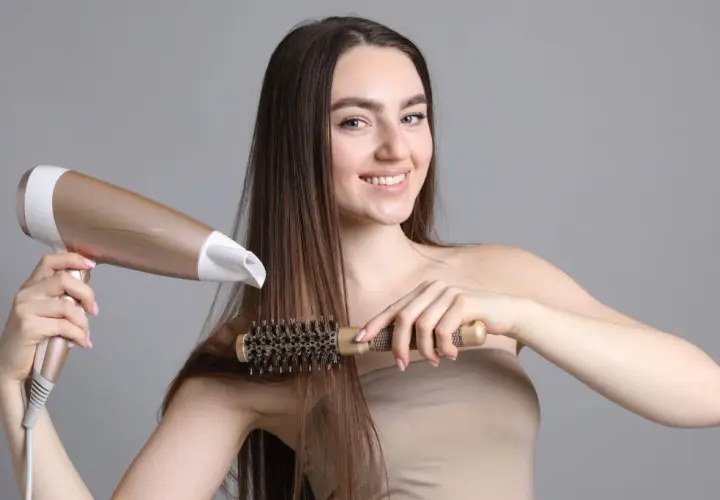 Kobieta suszy i modeluje włosy okrągłą szczotką i suszarką.