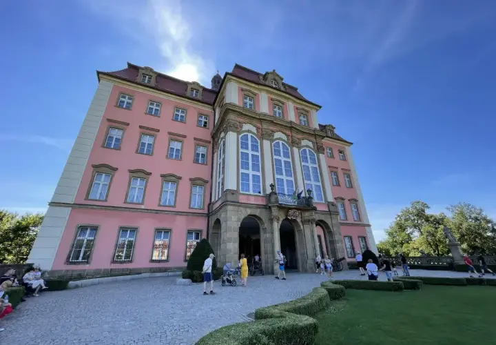 Zamek Książ, malowniczo położony, łatwy dojazd PKP. Turyści zwiedzają barokową budowlę w słoneczny dzień.