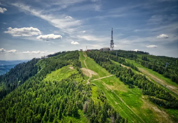 Widok na zielone **beskidzkie szczyty** z wieżą telekomunikacyjną na szczycie.