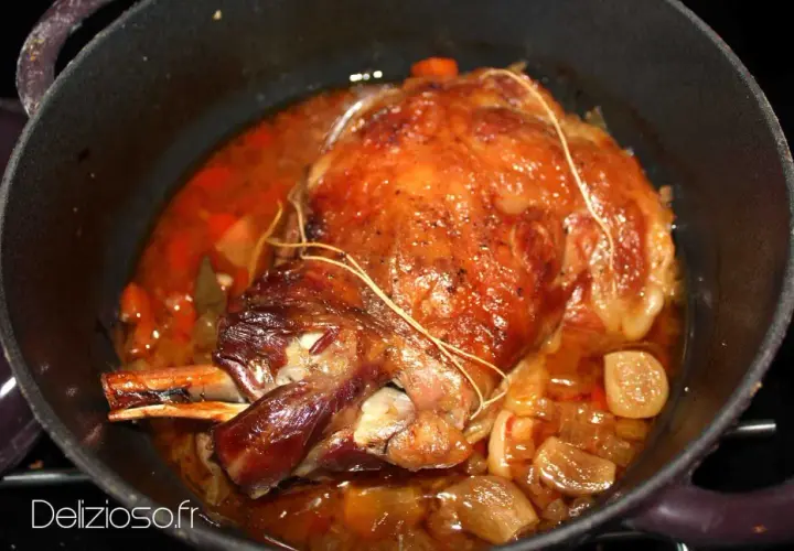 Une succulente épaule d'agneau rôtie dans sa cocotte, baignant dans un jus savoureux avec des oignons et des carottes.