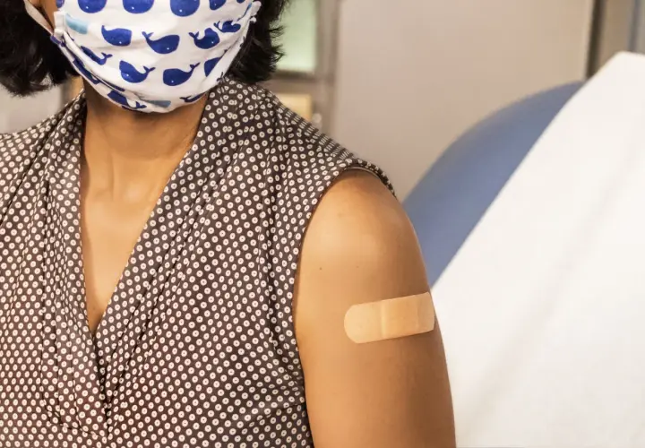 Osoba z maską na twarzy i plastrem na ramieniu po szczepieniu. Choć hpv szczepionka skutki uboczne są rzadkie, warto być świadomym.