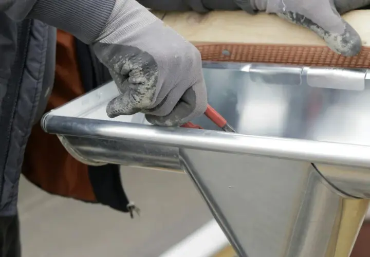 Hand mit Handschuh dichtet Dachrinne mit Werkzeug ab.