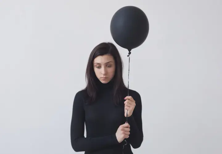 Donna con palloncino nero, espressione malinconica. Potrebbe rappresentare l'anedonia significato, la perdita di piacere.