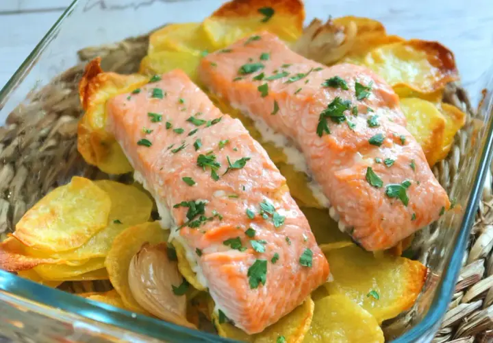 Dos filetes de salmón al horno con patatas doradas y perejil picado, listos para servir.