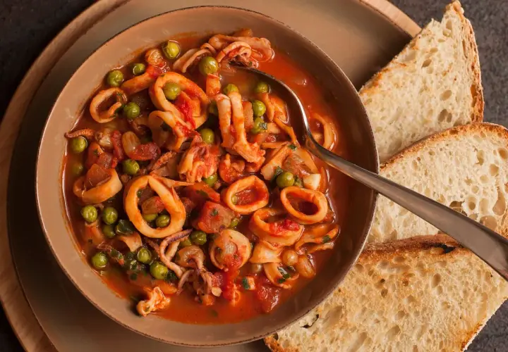 Calamari al sugo con piselli, un piatto saporito servito in una ciotola con pane tostato.