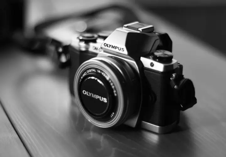 Prześwietlone zdjęcie aparatu Olympus OM-D. Srebrno-czarny korpus i obiektyw z napisem "OLYMPUS".