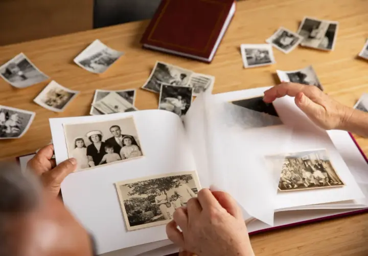 Wspomnienia wracają podczas wklejania zdjęć do albumu. Na stole leżą stare fotografie, a ręce starannie układają je na białych kartach.
