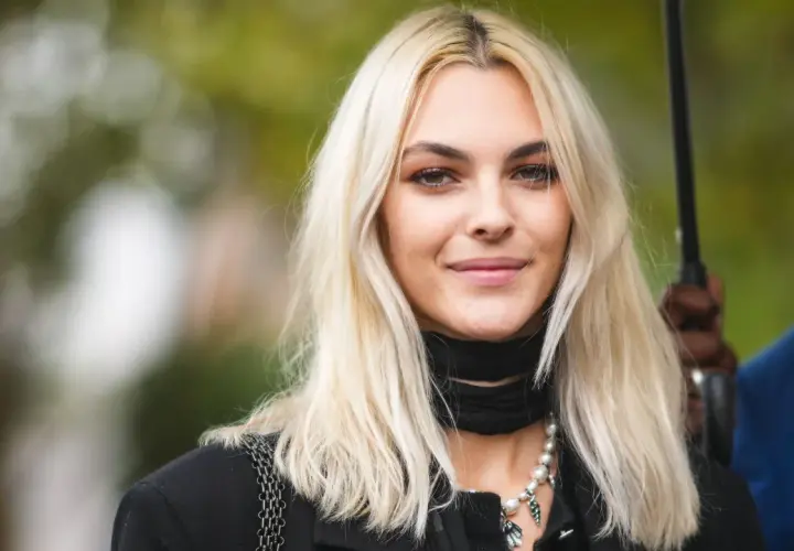 Mujer joven con pelo rubio platino, ¿qué color de pelo me favorece? Suave sonrisa, collar de perlas y pañuelo negro.