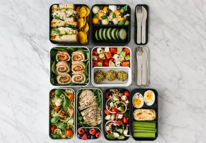A colorful bento box diet spread with sandwiches, fruit salad, chicken, pasta, and snacks, perfect for a healthy lunch.