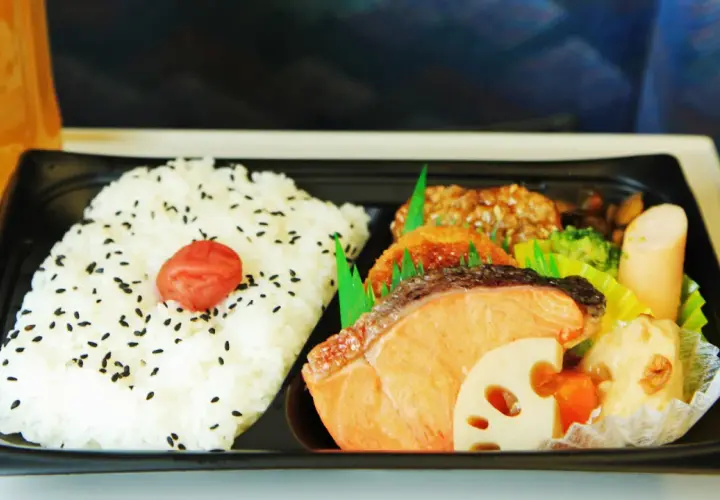 A delicious eki bento with rice, salmon, fried items, broccoli, and sausage, ready for a journey.