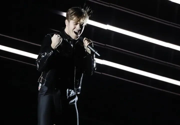 Benjamin Ingrosso levererar på scenen under Eurovision. Han sjunger passionerat med mikrofonen i handen, klädd i en glänsande svart jacka.