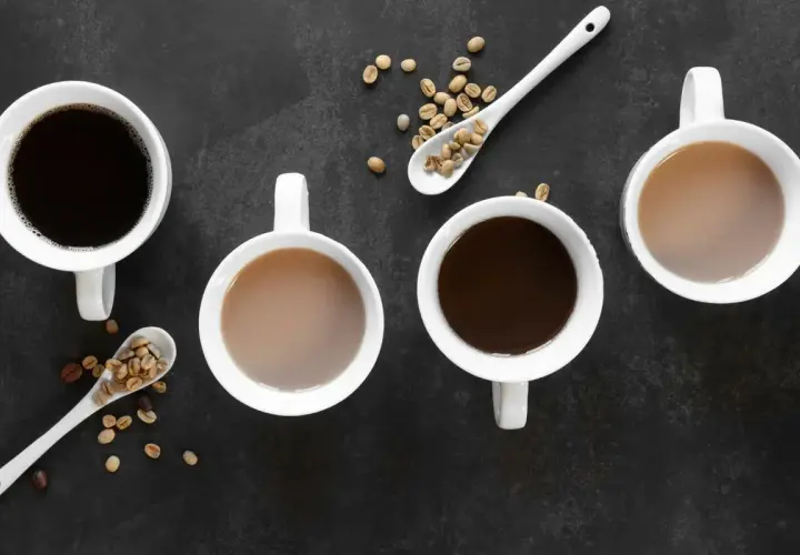 Vier Tassen Kaffee, zwei schwarz, zwei mit Milch, und Löffel mit Kaffeebohnen. Ein gemütlicher Tee-Teein-Moment.