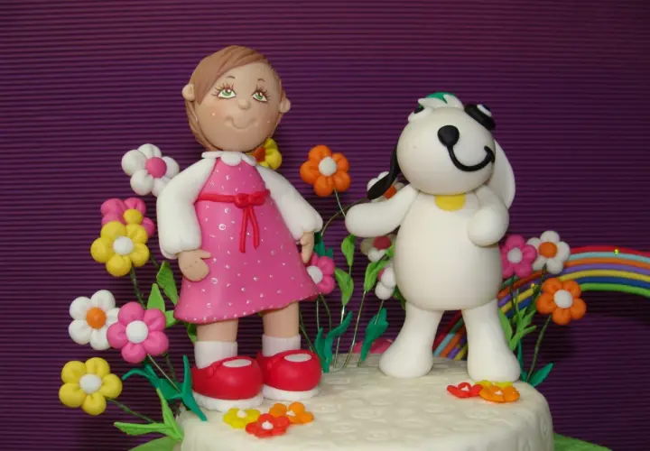 Figuras de porcelana fría: niña con vestido rosa y perro blanco rodeados de flores y un arcoíris.