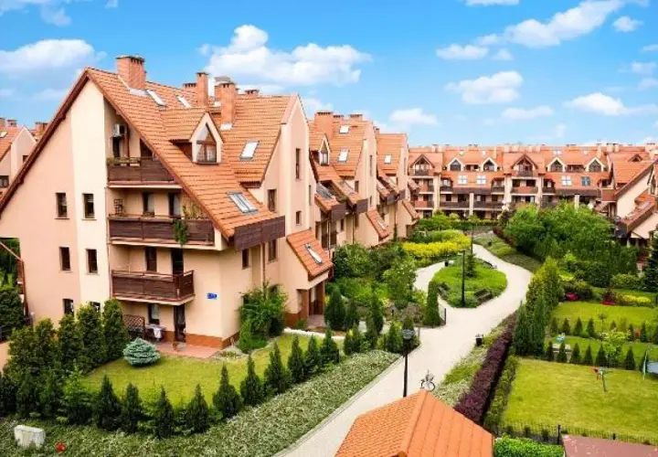 Osiedle Złota Podkowa: szeregowe domy z pomarańczowymi dachami, zadbane ogrody i kręte ścieżki tworzą sielski krajobraz.